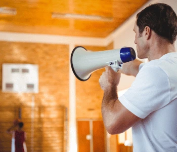 A person on a basketball court directs basketball player by using a megaphone with mic